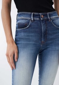 Jeans de tiro alto azul con un degradado desvanecido, que presentan un diseño clásico de cinco bolsillos, botón de cobre y costuras naranjas en contraste.