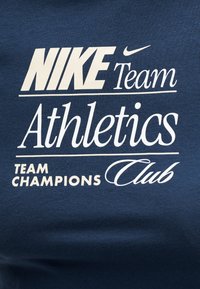 Λογότυπο Nike με το κείμενο «Team Athletics» και «Team Champions Club» τυπωμένο με λευκά γράμματα σε σκουρομπλε ύφασμα.