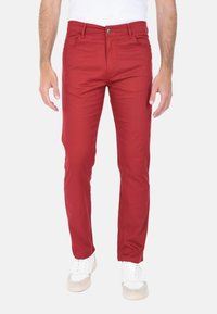 Pantaloni in cotone rosso con vestibilità slim, design a cinque tasche, chiusura con bottone e dettagli di cucitura visibili. Indossati con sneakers bianche.