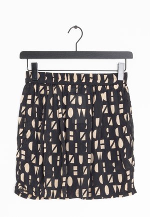 Jupe noire avec des formes géométriques abstraites beiges suspendue à un cintre noir avec des pinces sur fond blanc.