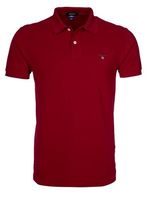 Kortærmet, rød poloshirt med krave, knaplukning og lille GANT-logo på venstre bryst. Skjorten vises på en ensfarvet baggrund.