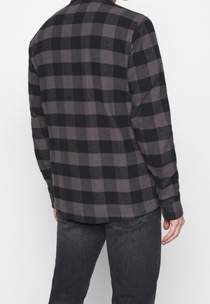 Camisa de franela a cuadros en negro y gris, con mangas largas, corte recto y puños de botón, hecha de un tejido suave y texturizado.