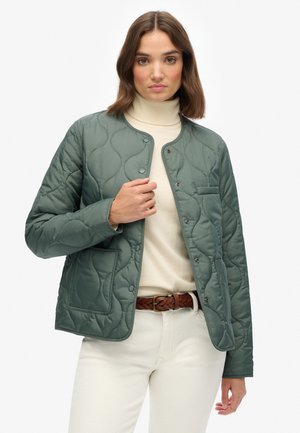 Gequilted groene jas met een ronde halslijn, drukknopen en een voorkoop. Draag het over een beige coltrui en crèmekleurige broek.