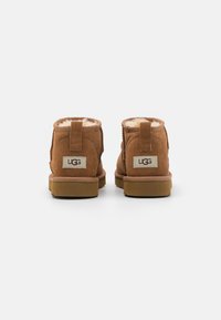 Brune suede ankelstøvler med blødt pelsfor, med en bageste trækklap og et mærke på hælen. Flad gummisål.