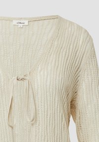 Beige gestrickte Strickjacke mit V-Ausschnitt und Bindeschnürung. Das Muster zeigt kleine vertikale Streifen und einen leichten, strukturierten Stoff.