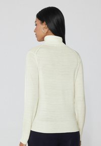 Suéter de cuello alto ligero color crema con mangas largas, puños y dobladillo acanalados. Presenta una textura suave y un diseño ajustado.