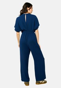 Navy blauwe jumpsuit met korte mouwen, een taillering en wijde benen; heeft een sleutelgatdetail aan de achterkant en is gemaakt van een zachte, vloeiende stof.
