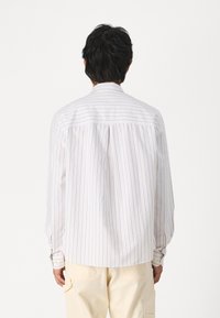 Camicia bianca con sottili righe verticali color beige. Maniche lunghe, polsini con bottone e orlo curvo. Tessuto morbido e vestibilità rilassata.