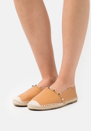 Scarpe slip-on in pelle color tan con punta rotonda, caratterizzate da borchie a forma di piramide lungo la parte superiore e una suola avvolta in juta. Texture complessiva liscia.