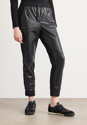 Black faux leather joggers with tapered ankles, elastic waistband, and contrasting ribbed cuffs. Paired with black sneakers.
