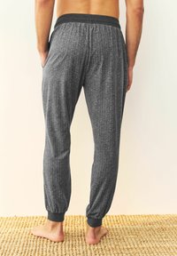 Graue Herringbone-Jogginghosen mit elastischem Bund, schmal zulaufenden Bündchen und seitlichen Taschen, von hinten gezeigt. Die gewebte Textur wirkt weich.