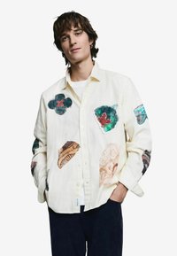 Heledast linast triiksärk, millel on erinevate tekstuuridega kangast lille- ja abstraktsete kujudena applikaadid, millel on selged mustrid ja värvid.