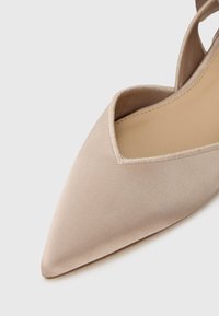 Μπεζ σατέν παπούτσι με μυτερή μύτη και V-σχήμα κοψίματος, με λεία υφή και μαλακή επένδυση, σχεδιασμένο με μ ινιμαλιστική αισθητική.