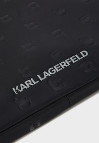 Black textured fabric featuring a subtle logo pattern. The embossed letters "KARL LAGERFELD" are prominently displayed in silver.