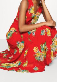 Röd blommig klänning med en flytande silhuett. Har färgglada blommönster i gult, grönt och blått. V-ringning, ärmlös design.