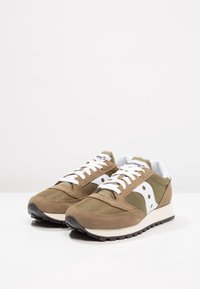 Béžové semišové a síťované sportovní boty s bílými akcenty a černými gumovými podrážkami. Obsahují bílé logo a tkaničky. Klasický design tenisek.