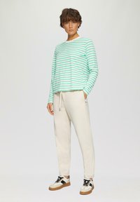 Gestreepte longsleeve top in mintgroen en wit, gecombineerd met beige joggers en zwart-witte sneakers. Casual pasvorm met zakken in de broek.