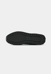 Svart sneaker såle med teksturert gummi for grep, med et rillemønster langs kantene. Slett overflate med merkevaredetalj.