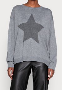 Sweat-shirt gris en tricot avec un motif d'étoile gris foncé sur le devant, encolure large et poignets côtelés. Associé à un pantalon en cuir noir.