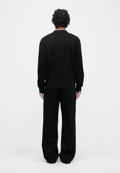 Suéter negro con cuello redondo y mangas largas, combinado con pantalones negros de corte holgado. Textura suave, diseño minimalista.