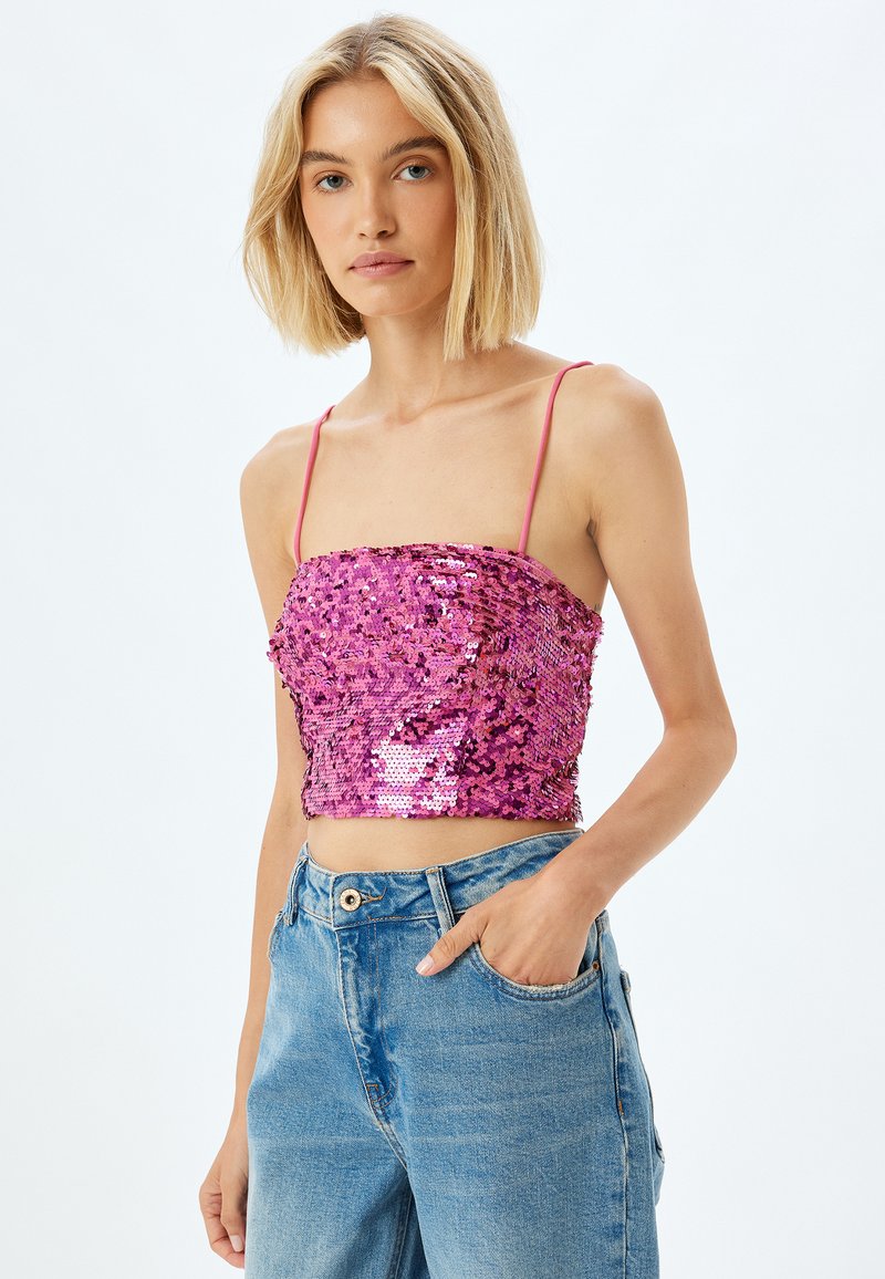 Lyserød pailletcrop-top med tynde justerbare stropper, der har en sammenkrøllet design og glat stof. Sammen med lys, højlaftede jeans.