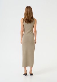 Khaki ärmelloses Strickkleid mit langer Silhouette, glatter Textur und geradem Schnitt, kombiniert mit schwarzen Absatzsandalen.