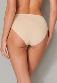 Perizoma beige a vita alta con una texture liscia, caratterizzato da un design senza cuciture e una fascia morbida, visto da dietro.