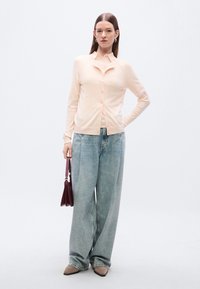 Ανοιχτό ροζ ζακέτα με στρογγυλή λαιμόκοψη και κούμπωμα με κουμπιά, συνδυασμένη με φαρδιά ανοιχτό μπλε τζιν παντελόνια και μπορντό τσάντα χειρός.