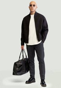 Svart texturerad jacka, vit skjorta, mörka byxor, svarta stövlar och en stor svart läderväska. Solglasögon fulländar outfiten.