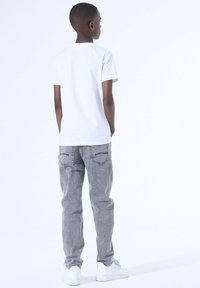 Witte t-shirt met korte mouwen gecombineerd met grijze jeans met achterzakken en een losse pasvorm, afgemaakt met witte sneakers.