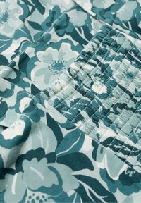 Květinová látka v různých odstínech azurové a bílé barvy. Obsahuje shromážděnou texturu v sekcích, s velkými květinovými vzory a zelenými listy.