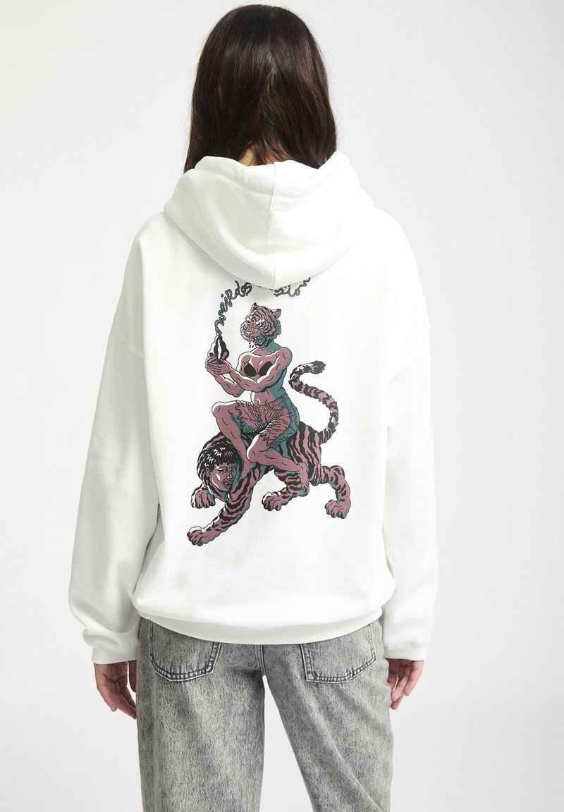 Vit hoodie med en djärv grafisk design av en figur som rider på en tiger, med rosa och tealfärgade accenter. Tillverkad av mjukt, texturerat tyg.