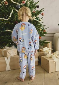 Set de pijamale de culoare albastru deschis, cu personaje cartoon jucăușe purtând căciuli de Moș Crăciun. Fabricat dintr-un material moale, cu talie elastică și mâneci strânse.