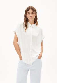 White short-sleeve button-up shirt made of smooth fabric, with a classic collar and relaxed fit, paired with light blue trousers.