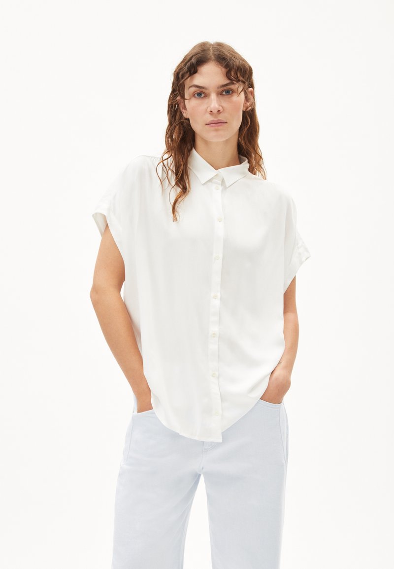 White short-sleeve button-up shirt made of smooth fabric, with a classic collar and relaxed fit, paired with light blue trousers.