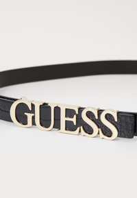 Czarny pasek z sztucznej skóry z zapięciem w kolorze złotym z logo "GUESS", o teksturowanej powierzchni i eleganckim designie.