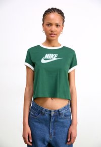 Green cropped t-shirt with white round neckline and sleeve cuffs, featuring a white Nike logo across the chest, paired with blue denim jeans.