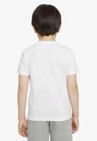 T-shirt bianca in cotone con maniche corte, scollo rotondo, vista posteriore. La maglietta è abbinata a pantaloncini grigi.