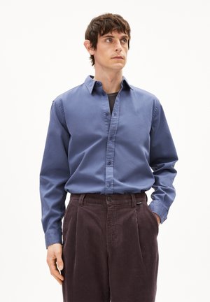 Blauw button-up shirt van katoen, met een kraag en lange mouwen. Gecombineerd met bruine corduroy broek, met verticale ribbels en plooien.