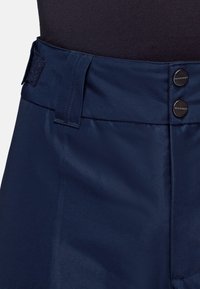 Marineblauwe outdoorbroeken met een zachte, lichte textuur, voorzien van een knoopsluiting en klittenbandsluiting voor aanpassing in de taille.