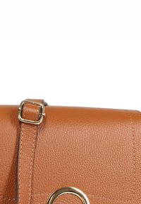 Braune Leder-Handtasche mit strukturierter Oberfläche, ausgestattet mit einem kreisförmigen Akzent in Gold und einem flachen Tragegurt mit verstellbarem Schnallenverschluss.