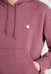 Støvet rosa hettegensser laget av myk bomullsblanding, med en frontlomme, snøring og en liten hvit logo på brystet.