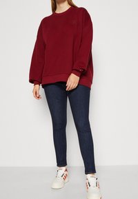 Sweatshirt oversize bourgogne avec col rond, poignets et ourlet côtelés, associé à un jean skinny bleu foncé et des baskets blanches et rouges.