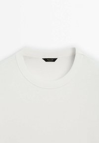 T-shirt blanc à manches courtes avec un col rond côtelé. Texture de tissu douce, sans motifs visibles, et une étiquette de marque noire au cou.