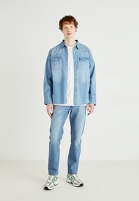Ljusblå denimskjorta med långa ärmar, knäppning fram, två bröstfickor; kombinerad med ljusblå jeans och mönstrade sportskor.