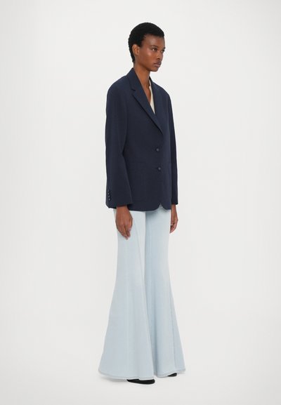Navy blazer with a tailored fit and two-button closure, paired with light blue flared trousers. Smooth fabric and structured design.
