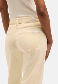 Pantaloni in corduroy gialli con vita aderente, due tasche posteriori e una texture sottile. Un'etichetta bianca è visibile sulla cintura.