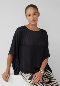 Haut en soie noire avec une silhouette large et fluide et des manches courtes. Présente un col rond et un aspect satin, associé à un pantalon à motifs.