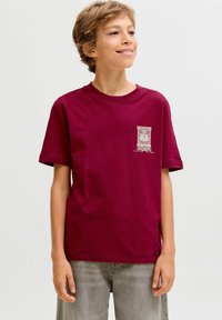 Burgundijas krāsas kokvilnas t-krekls ar īsām piedurknēm, ar baltu grafisku apdruku kreisajā krūtīs, apaļu izgriezumu un brīvu piegriezumu.