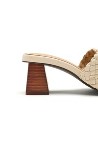 Sandalia deslizante de cuero beige trenzado con puntera redondeada, que presenta un tacón de bloque de madera apilada texturizado. Diseño sofisticado y moderno.